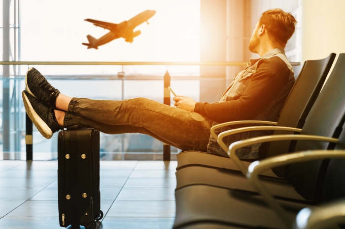 un hombre sentado cómodamente en la sala de espera del aeropuerto viendo despegar un avión, consejos para organizar mejor su viaje en avión