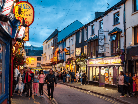 Atardecer ocupado en la ciudad de Killarney, uno de los mejores lugares para visitar en Irlanda, donde se ve a la gente despertarse a lo largo de las aceras junto a pubs y restaurantes.