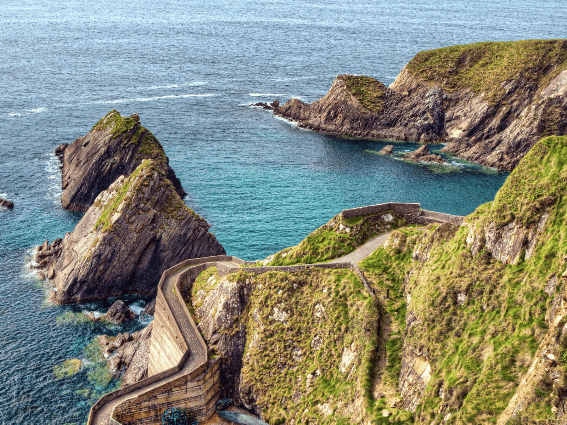Camino sinuoso en Dunquin Pier y formaciones rocosas únicas sobre un mar tranquilo en la península de Dingle, una pieza sobre los mejores lugares para visitar en Irlanda