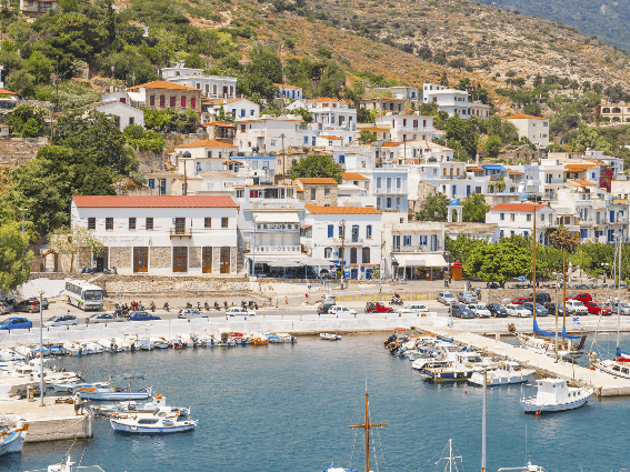 Coches aparcados en una carretera costera y barcos atracados en un puerto de la ciudad de Agios Kirikos en la isla de Ikaria, una de las mejores islas de Grecia para visitar