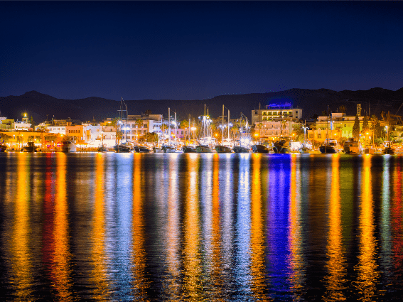 Colorida luz nocturna en un puesto en la isla de Kos, una pieza sobre las mejores islas de Grecia para visitar, donde los barcos están atracados