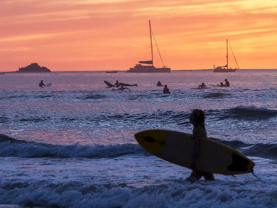 Silueta de botes y surfistas remando durante la dulce puesta de sol en Playa Tamarindo, una pieza en las mejores playas de Costa Rica