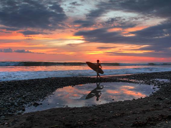 Silueta de un surfista corriendo y olas altas en una hermosa puesta de sol en la costa rocosa de Playa Dominical, una de las mejores playas de Costa Rica