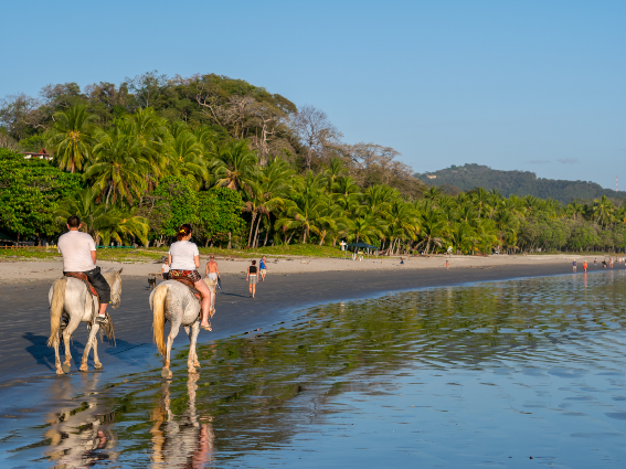 Turistas cabalgando en la playa de Samara, una de las mejores playas de Costa Rica que también tiene arena negra