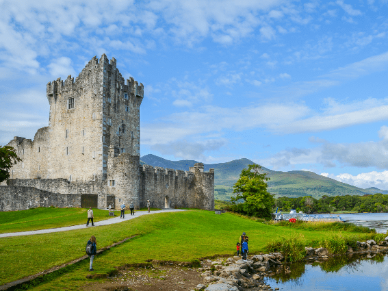 Turistas deambulando por el patio verde del castillo de Ross en Killarney, uno de los mejores lugares para visitar en Irlanda