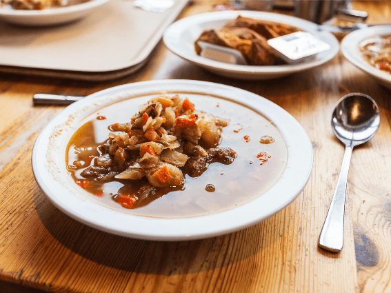 Un plato de sopa de cordero islandesa Kjotsupa tradicional con una cuchara y otros platos borrosos en el fondo en una mesa de madera en Reykjavík Kitchen, conocido como uno de los mejores restaurantes de Islandia