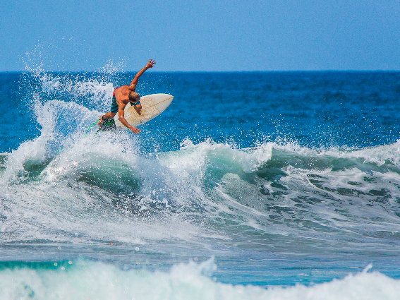 Un surfista masculino profesional que disfruta de una de las mejores cosas que hacer en Costa Rica, vistiendo pantalones cortos de tabla de rayas azules montando enormes olas