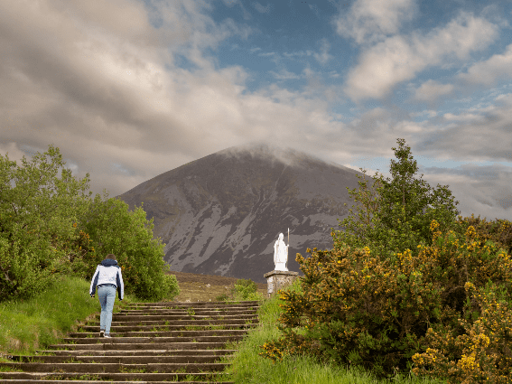 Una joven subiendo escaleras hasta el pico nublado Croagh Patrick, uno de los mejores lugares para visitar en Irlanda