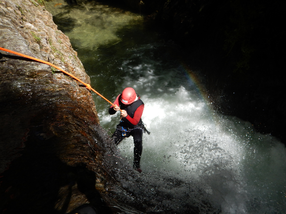 Una persona con un casco rojo sosteniendo fuertemente una cuerda naranja mientras atraviesa una cascada, una de las mejores cosas que hacer en Costa Rica