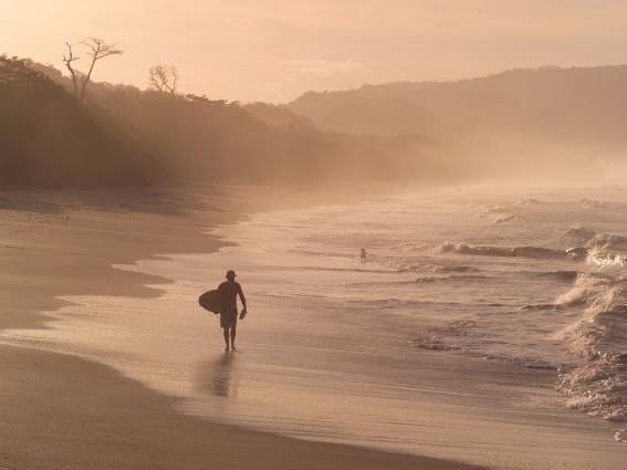 Único de un surfista caminando en uno de los mejores lugares de Costa Rica para visitar, Malpaís, en un día brumoso