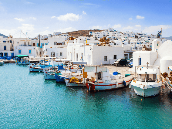 Varios barcos de pesca atracaron en la costa de Naousa Village en la isla de Paros, una de las mejores islas de Grecia para visitar, donde los automóviles están estacionados cerca de sus emblemáticas casas blancas.