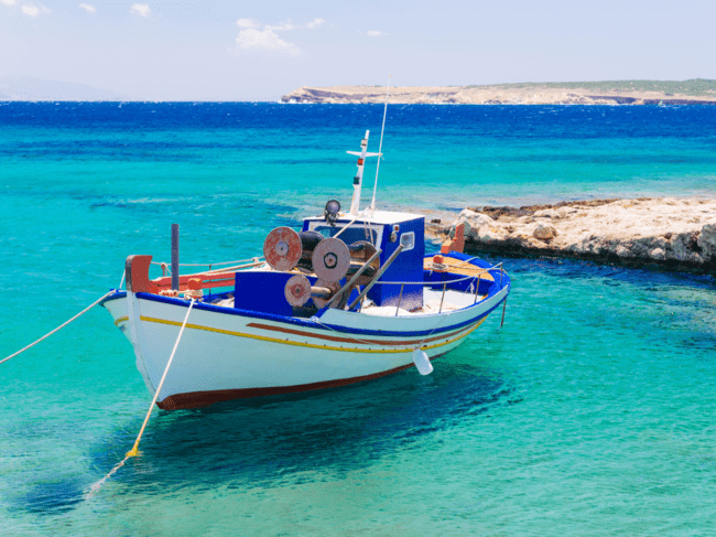 Viejo barco de pesca azul fotografiado en el agua clara durante el mejor momento para visitar Santorini