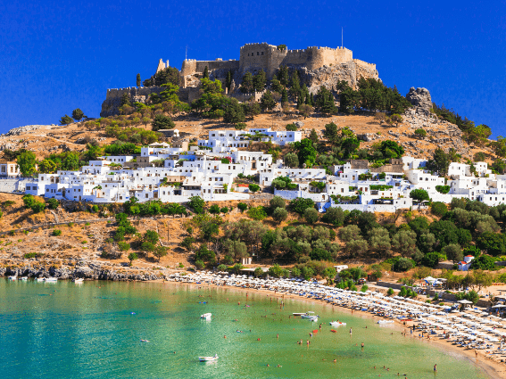Y el antiguo castillo sentado en el pico de una montaña y los edificios residenciales y comerciales blancos en una de las mejores islas de Grecia para visitar, la isla de Rodas con su concurrida playa durante la temporada de verano.